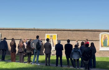 Grupo de personas, vestido en abrigos y vaqueros, observando atentos un evento religioso al aire libre en un entorno verde.