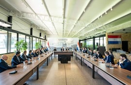 César Barreto y otros hombres en traje, rodeados de banderas paraguayas en un ambiente formal de reunión.
