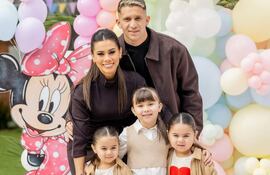 Jorge Morel sonríe junto a una mujer en atuendo oscuro y tres niñas con camisetas de Disney, rodeados de globos coloridos.