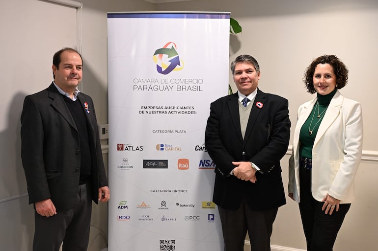 Jorge Garicoche y Juan Carlos Boggino en trajes, Carolina Vergara en blazer, posando alegres frente a banner de auspiciantes.