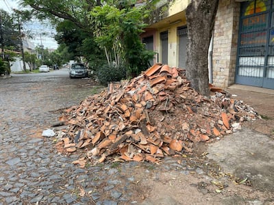 Escena urbana con montículo de escombros y vehículos estacionados en una calle poco transitada.