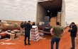 Agentes de seguridad revisan un camión de carga con cajas desordenadas en un terreno de tierra roja, mientras examinan el robo.