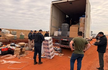 Agentes de seguridad revisan un camión de carga con cajas desordenadas en un terreno de tierra roja, mientras examinan el robo.