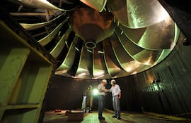 El tamaño de los técnicos y el de la pieza de una de las turbinas de la central hidroeléctrica.