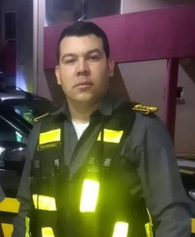 Hombre en uniforme de seguridad de camisa gris y chaleco amarillo en un entorno urbano. Expresión neutral, posando para la cámara.