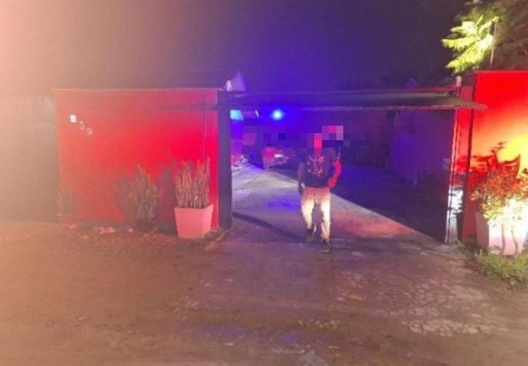Hombre con camiseta oscura y pantalones claros avanza hacia la cámara en un ambiente iluminado con luces rojas y azules.