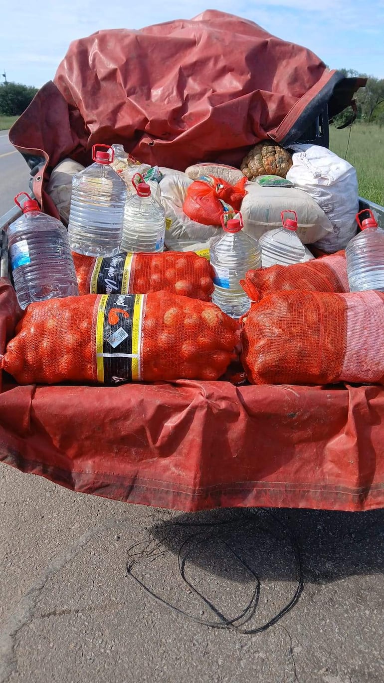 Vehículo de carga con lona roja estacionado, llevando sacos rojos y botellas de agua en una ruta rural.