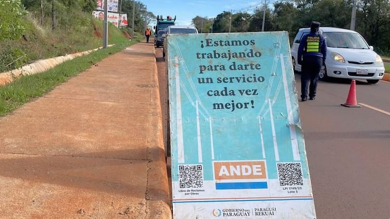 Agente de la Policía Municipal en chaleco reflectante dirige el tráfico junto a un cartel de la ANDE sobre trabajos en la calle.