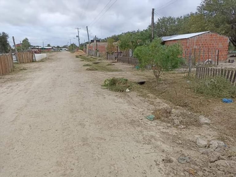 Calle de tierra en un ambiente rural, flanqueada por construcciones de ladrillo y vegetación recortada.