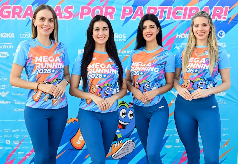 Cuatro mujeres sonrientes vestidas con camisetas azules y naranjas del Mega Running 2026+ posan juntas en un ambiente festivo.