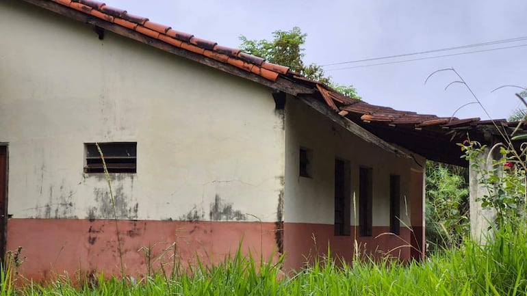 Construcción deteriorada de USF con techo dañado, paredes manchadas y vegetación densa alrededor, en un ambiente de abandono.