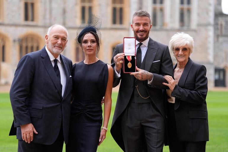 David Beckham junto a su esposa Victoria Beckham y sus padres, Ted y Sandra, tras ser nombrado Caballero. (Andrew Matthews / POOL / AFP)