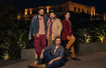 Cuatro hombres posan en un evento al aire libre, vestidos con chaquetas y pantalones coloridos, en un ambiente iluminado y relajado.