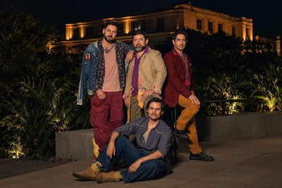 Cuatro hombres posan en un evento al aire libre, vestidos con chaquetas y pantalones coloridos, en un ambiente iluminado y relajado.