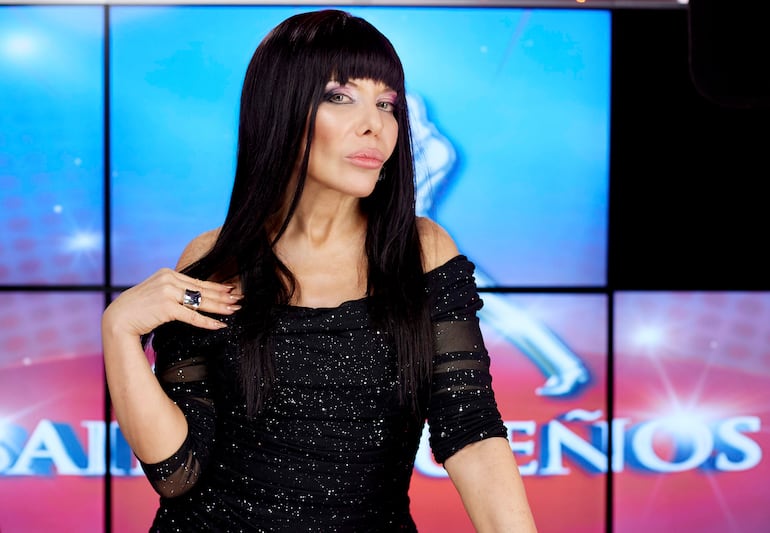 Cecilia Roth en vestido negro brillante, posando con expresión carismática en un set de televisión colorido.