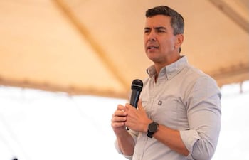 Hombre con micrófono gesticulando bajo una carpa, vistiendo camisa clara, mientras se lleva a cabo un evento al aire libre.