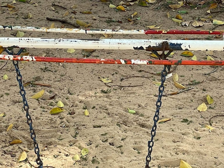 Estructura de barras de gimnasio en un área de arena cubierta de hojas secas en un parque.