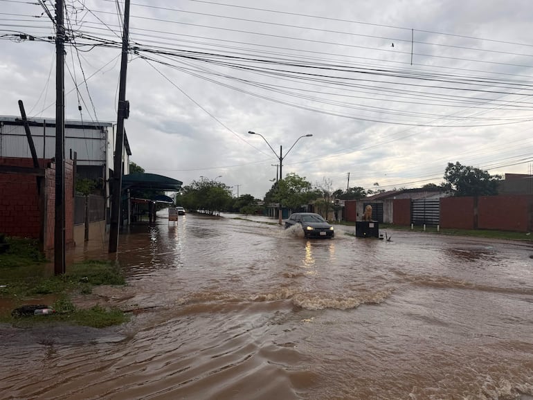 Coche circulando en calle inundada, rodeado de casas con techo a la vista, bajo un cielo nublado.