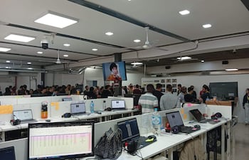Varias personas están en un aula, conversando y usando computadoras, en un ambiente de actividad colaborativa.