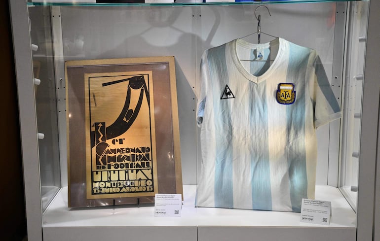 Una camiseta de Argentina vestida por el fallecido Diego Maradona durante la Copa del Mundo de 1986 y un cartel litográfico monocromático de la Copa del Mundo inaugural de 1930, realizado por el diseñador uruguayo Guillermo Laborde, se exhiben antes de su subasta en Heritage Auctions en Beverly Hills, California.