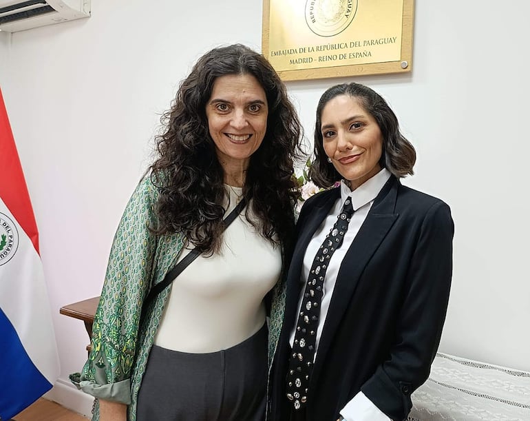 Dos mujeres sonrientes conversan en la Embajada de Paraguay. Una viste chaqueta verde, la otra un abrigo negro.