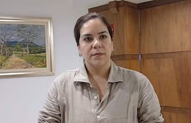 Johanna Ortega en camisa clara, reflexionando en oficina con pared de madera y pintura de paisaje al fondo.