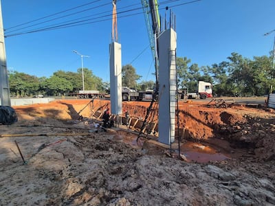 Obra en proceso con grúa y columnas de concreto, entorno de construcción con tierra y herramientas.