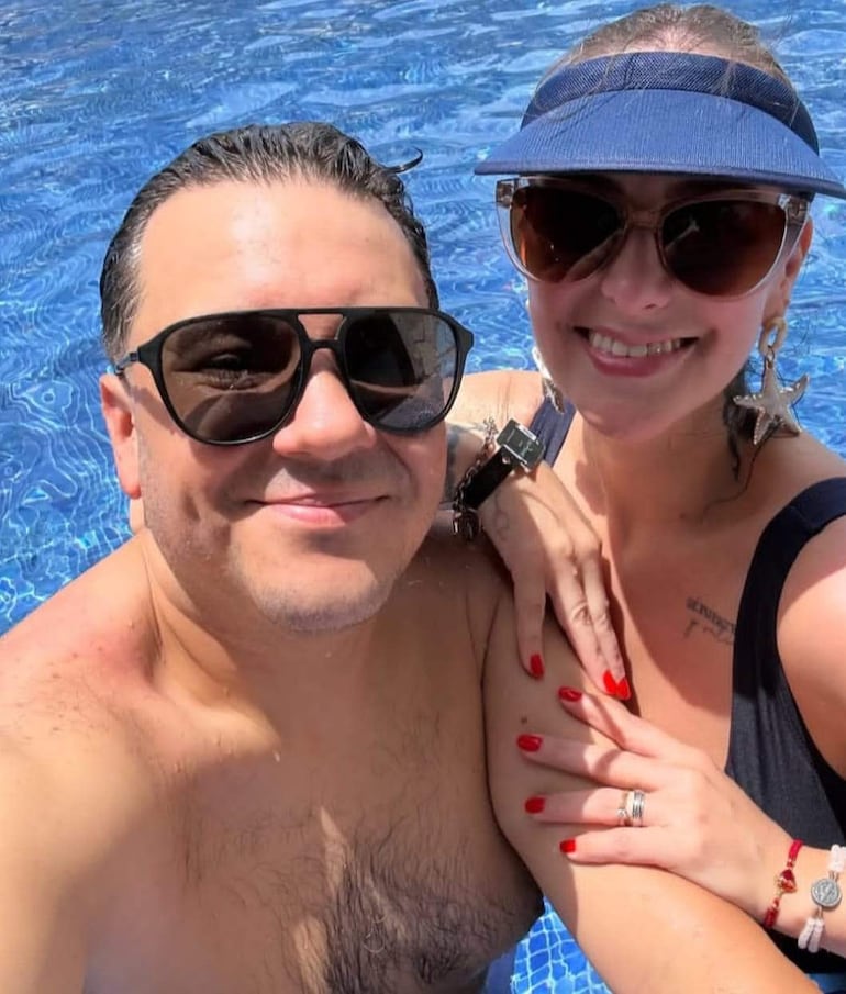 Hombre sin camiseta con gafas de sol y mujer con traje de baño negro y visera azul, sonriendo en la piscina.