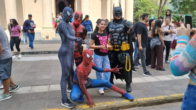 Niña con camiseta negra 'I just wonder' sonríe junto a personajes disfrazados de Spider-Man, Deadpool y Batman en un ambiente festivo.