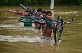 Varias personas con bicicletas cruzan una zona inundada de la localidad de Kalapani, en el estado indio de Assam.