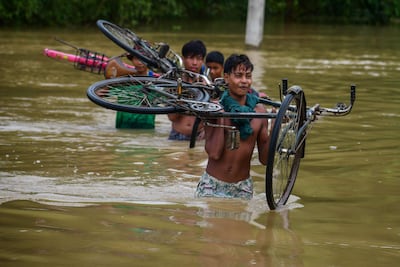 Varias personas con bicicletas cruzan una zona inundada de la localidad de Kalapani, en el estado indio de Assam.