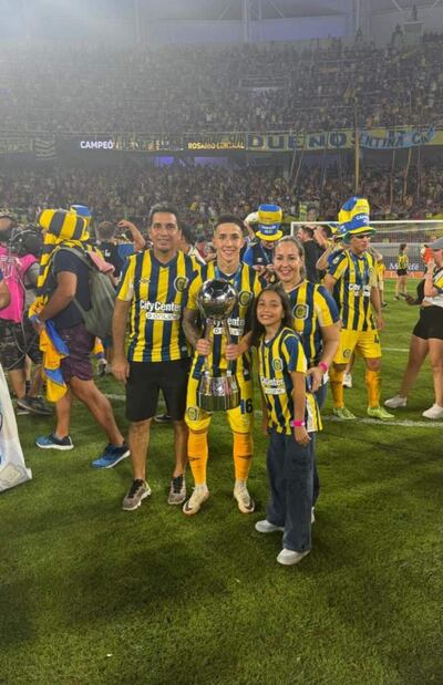 Alan Rodríguez exhibe el trofeo de campeón rodeado de sus familiares en el campo de juego.