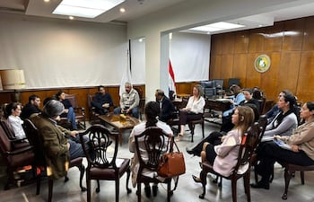 Reunión formal con Isaías Fretes, hombres y mujeres vestidos de forma semi-formal en ambiente de oficina con decoración de madera.