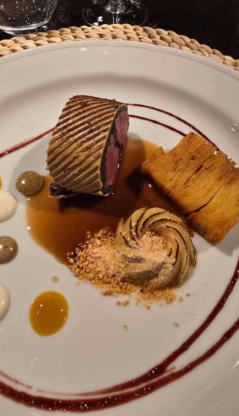 Plato decorativo con rollo de carne y salsas variadas, dispuesto en fondo oscuro.