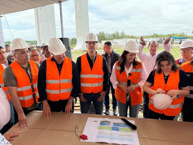 Santiago Peña Palacios y Claudia Centurión hablan en evento al aire libre con chalecos de seguridad naranja y cascos en un sitio de construcción.