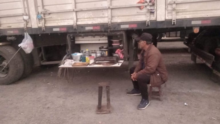 Hombre con cabello oscuro y lentes, vestido con camiseta negra y chaqueta marrón, frente a un camión con herramientas de cocina.