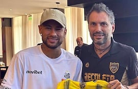 Luis Vidal sostiene una camiseta amarilla con 'NEYMAR JR' mientras sonríe en un evento con Neymar presente.