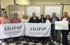 Ocho mujeres sostienen banderas de la ADJPJP y un cartel que dice 'Resolución ya', en una protesta para acceder a la jubilación.