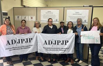 Ocho mujeres sostienen banderas de la ADJPJP y un cartel que dice 'Resolución ya', en una protesta para acceder a la jubilación.
