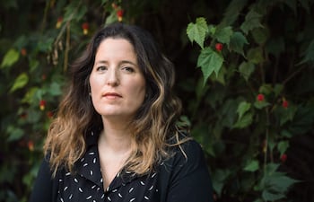 Agustina Bazterrica con cabello largo y ondulado, vestida con camisa negra y patrón blanco, en un entorno natural con hojas verdes.