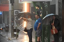 Dos hombres y dos mujeres bajo paraguas en una lluviosa Costanera Norte, reflejando el agua en la acera.