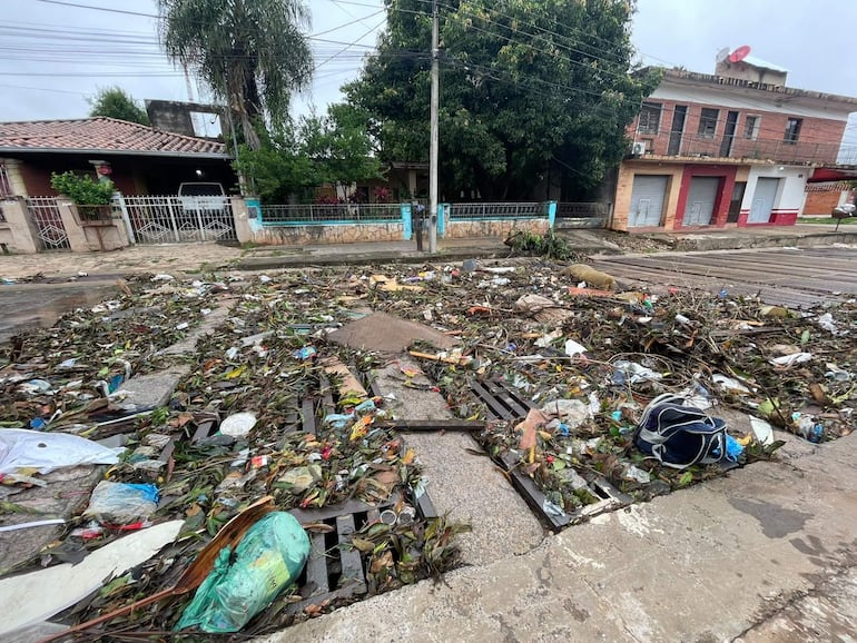 Escena urbana afectada por inundaciones con basura y desechos plásticos en una calle asfaltada.