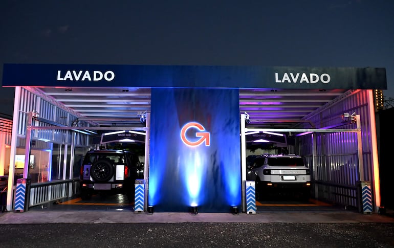 Instalación moderna de lavado de autos, con vehículos oscuro y claro en el área de servicio, ambiente iluminado y atractivo.