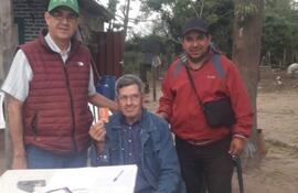 Héctor Cáceres, (Chaleco granate y quepis verde) candidato de la ANR a la Intendencia de Humaitá, posa junto a un adulto mayor y un candidato a Concejal durante la entrega de tarjetas para el cobro de la pensión destinada a personas mayores.