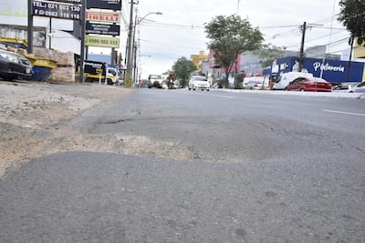 Calle con bache visible y vehículos en movimiento, sin presencia de personas, en un entorno urbano comercial.