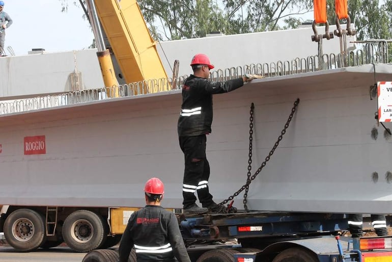 Cinco hombres con cascos de seguridad trabajan en la construcción, un operando una grúa y otros supervisando el izado de una viga.