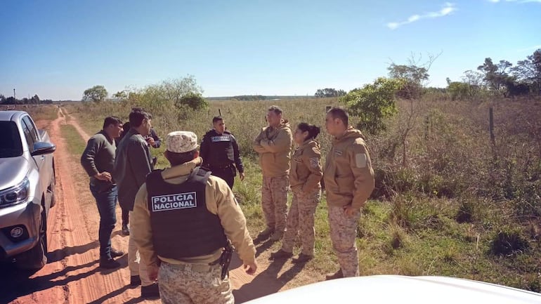 Cuatro policías en uniformes conversan con dos hombres en un entorno rural despejado.
