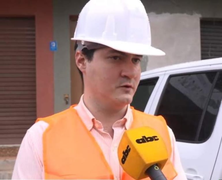 Alejandro Bordón con casco blanco y chaleco reflectante naranja, hablando ante un micrófono durante una entrevista en un área urbana.