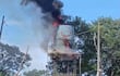 Tanque de agua en llamas con densa columna de humo negro en un entorno de vegetación y postes de electricidad.