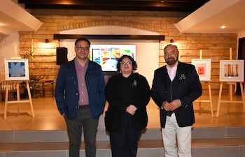 Pierre-Christian Soccoja con cabello rizado y gafas, junto a dos hombres; ambiente elegante con obras de arte en exhibición.